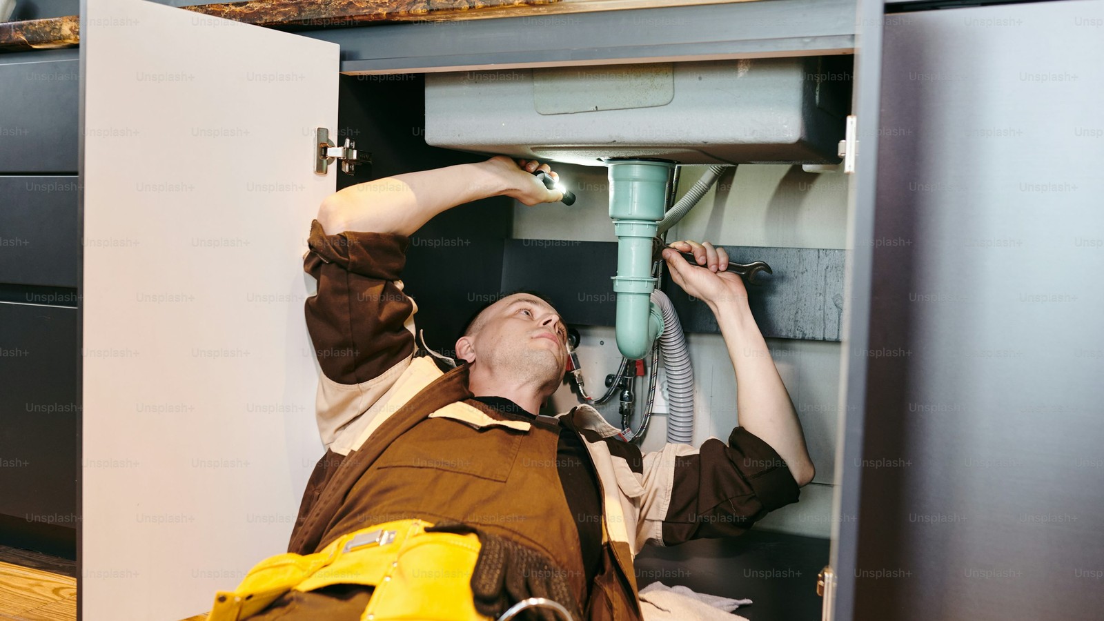 Plumber repairing residential plumbing under a sink
